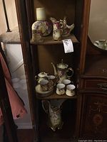 Photo showing multiple pieces of hand painted Nippon china arranged on shelving including teapot, cups, saucers, creamer, sugar bowl, vases, and decorative bowl