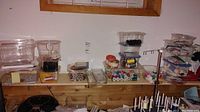 Shelf with assorted transparent containers holding various sewing threads, beads, and strings in multiple colors.