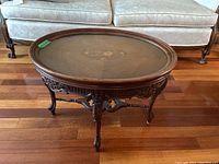 Full view of the vintage oval wood coffee table with glossy floral inlay under glass top showing the carved apron and cabriole legs.