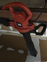 Close-up photo of one Black & Decker electric yard blower showing orange and black housing, curved handle, and attached blowing tube.