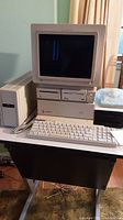 Frontal view of Apple IIgs system unit stacked with CRT monitor, keyboard in front and AE HD drive on right