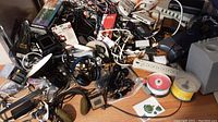 Overall view of the mixed electronics assortment with various cables, headphones, power strips, and CDs sprawled on a wooden surface.