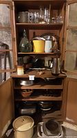 Full view of cabinet shelves filled with glassware on top shelves and metal containers and cookware below