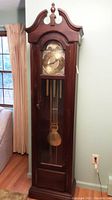 Full front view of vintage wooden grandfather clock with glass door showing pendulum and weights inside.