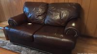 Front view of dark brown leather loveseat with nailhead trim and plush back cushions.