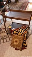 Mid century modern rolling cart wooden top and metal legs with wheels, small '60s style rug and decorative floral pillow under the cart