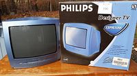 Front view of the blue Philips Designer TV model 13PR11M alongside its original box.