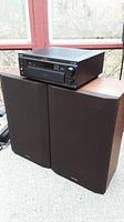 Sony STR-DA55ES receiver on top of two large Optimus 40-4032A speakers with cloth grills and wood finish cabinets.