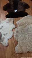 Photo showing all three rugs on wooden floor: dark brown rectangular rug, cream-colored slightly worn rug, and smaller cream and brown sheepskin rug
