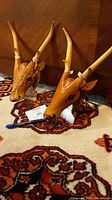 Pair of wood carved gazelle heads with red beaded eyes on mounted boards shown on carpet.