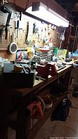 Workbench cluttered with various hand tools, containers, and workshop supplies against pegboard background