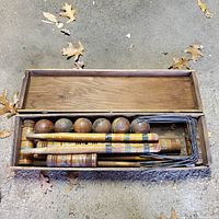 Closed wooden box open to show croquet balls, mallets and wickets inside