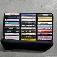 Photo showing 24 cassette tapes stacked in the double-sided case, including artists like Perry Como, Elvis Presley, Nat King Cole, Kenny Rogers, Dolly Parton, Freddy Fender.