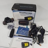 Photo showing Garmin box with device and accessories arranged around it including GPS unit, remote control, cables, CD, user manual, mounting hardware, and pouch.