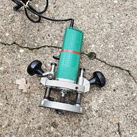 Image showing a green Grizzly power router with silver metal base and black knobs, placed on a concrete surface.