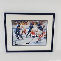 Framed print showing young hockey players in action on ice rink, with dark blue frame.