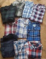 Ten folded men's flannel long sleeve shirts arranged on a floor, showing assorted plaid patterns and colors.