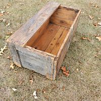 Side view of open wooden crate showing interior with wood planks and visible nail heads, placed on grass.