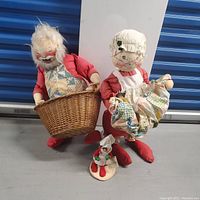 Full lot view showing Santa Claus doll holding basket, Mrs. Claus doll holding a quilt, and small elf doll on floor.