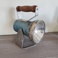 Blue cylindrical vintage railroad lantern with large glass lens and wooden handle, mounted on metal stand with star cutouts.