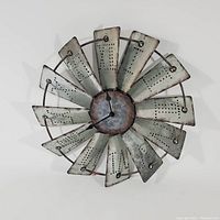Front view of the metal windmill wall clock with twelve weathered metal blades and central clock.face
