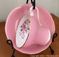 Front angled view showing the pink corset styled teacup with floral pattern inside and gold rim, resting on matching saucer displayed on a black stand.