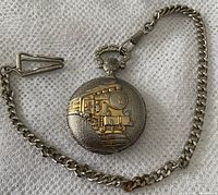 Front view of silver-colored pocket watch with gold train motif and attached chain on white textured fabric