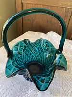 Front side view of deep bluish turquoise basket showing ruffle edges and diamond patterned glass with handle attached.