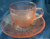 Photo of pink depression glass teacup and saucer with intricate textured pattern shown from the side