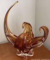 Front angle showing the tall curved arm and three shorter curled arms of the amber glass sculpture on a flat surface.