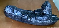Full view of Inuit hunter seated in kayak with spear and fish visible on the right side, carved in dark soapstone.