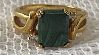 Close-up front view of gold-colored ring with rectangular green malachite stone and two small clear rhinestones on either side.