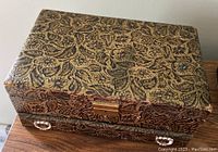 Top and angled front view of Lady Buxton large rectangular jewelry chest with gold and black floral paisley embossing, showing intact latch and ring-pull handles on drawer
