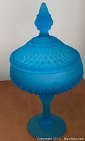 Side angle of blue satin glass lidded compote showcasing diamond point textured pattern and pointed finial.