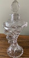 Full view of the vintage glass perfume bottle with stopper on top, showing the sculpted man on the side and ruffled design around the neck.