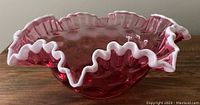 Side view of pink cranberry glass bowl showing ruffled white crested edge.