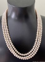 Full view of the triple strand pearl necklace displayed on black mannequin showing color and layering of the strands.