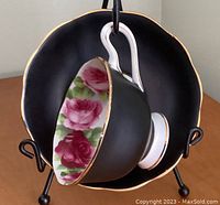 Teacup inside saucer showing the black matte exterior with pink rose floral interior and gold trim