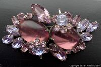 Close-up image of the Sherman brooch showing large pink oval cabochons surrounded by purple rhinestones on black background.