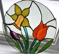 Front view of the 10 inch round stained glass panel with a yellow daffodil, orange tulip, and purple tulip on a textured clear glass background.