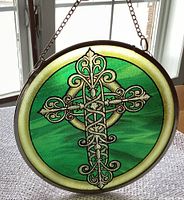 Circular stained glass hanging featuring a Celtic cross design shown front view with natural light from window.