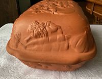 Photo of side view of terra cotta roaster showing embossed vegetables design on lid and sides