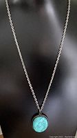 Full view of vintage oval turquoise pendant on silver colored chain against black background.