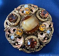 Close-up view of the round vintage brooch highlighting amber rhinestones, faux pearls, marbled cabochon, and detailed filigree metalwork.