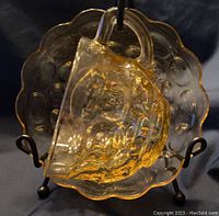 Amber depression glass teacup placed on matching saucer, showing dot pattern and scalloped edges under lighting.