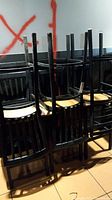 Six black metal framed bar stools with wooden seats stacked upside down in a row. The stools have tall backrests with vertical slats and show signs of wear.