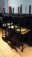 Six metal frame bar stools stacked upside down in a room with tiled floor and dark wall.