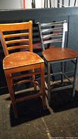 Photo showing both bar stools side by side: the left is solid wood with visible wear, the right is metal framed with wooden seat and metal slatted backrest.