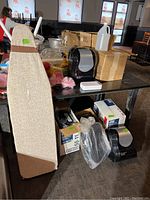 Shows ironing board leaning against table with hand towel dispensers, cleaning brushes, phone sanitizer, and boxed items underneath