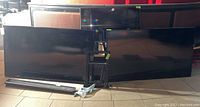 Three flat-screen TVs shown: two larger (60-inch) and one smaller (46-inch) all black with a digital sign and TV stand parts in front.